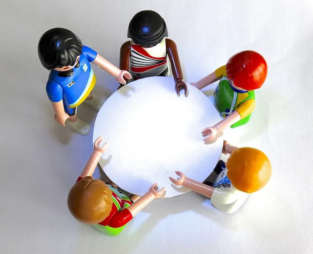 Un grupo de figuras de Playmobil están sentadas alrededor de una mesa blanca.