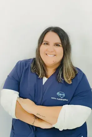 Una mujer con un uniforme azul está de pie con los brazos cruzados y sonriendo.