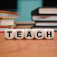 La palabra enseñar está escrita en dados sobre una mesa de madera.